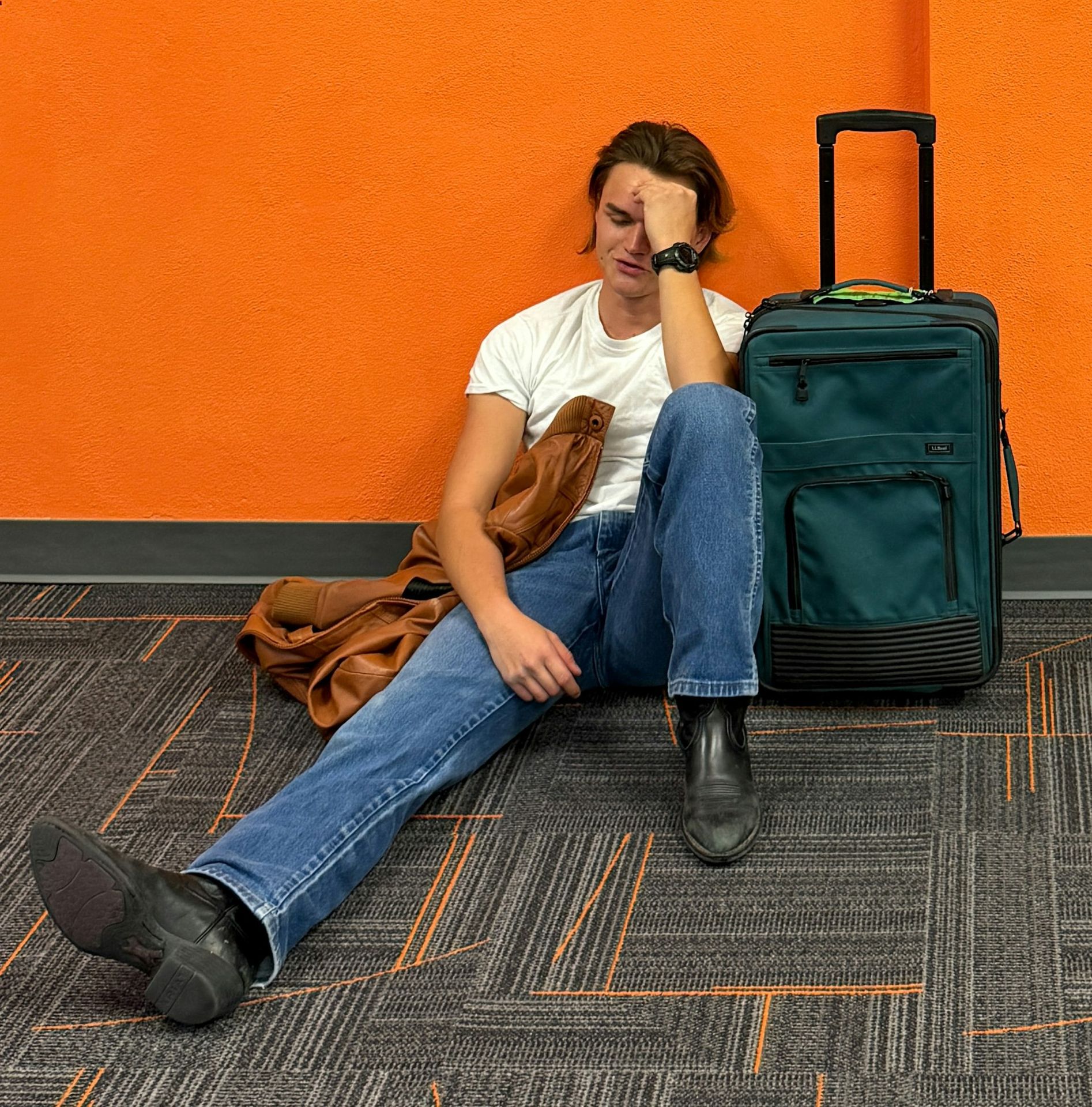 Man sitting on floor with luggage, looking tired.